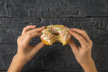 Çocuğun elleri, tahta bir arka planda ısırılmış bir çörek tutuyor. Popüler hamur işleri.