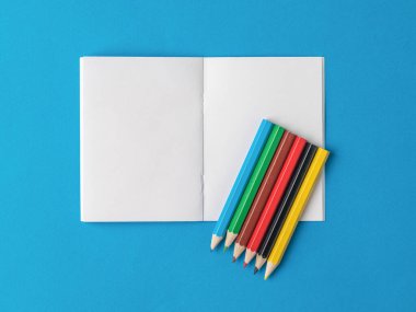 Mavi arka planda açık bir deftere altı renkli kalem. Kırtasiye malzemeleri ve okul malzemeleri..