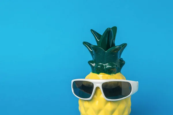 Pineapple wearing black glasses on a blue background. Summer concept.