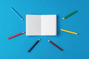 Açık bir defterin etrafında duran renkli kalemler. Kırtasiye malzemeleri ve okul malzemeleri..