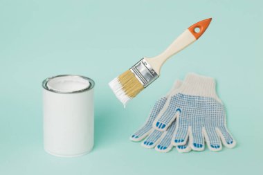 Eldivenlerin ve boya kutularının arka planında beyaz boya olan yüzen fırça. Resim çalışmalarının yürütülmesi.