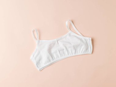 Hafif pastel arka planda, basit bir beyaz kadın sütyeni. Kızlar için iç çamaşırı..
