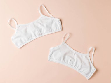 Hafif pastel arka planda iki basit pamuklu kadın sütyeni. Kızlar için iç çamaşırı..