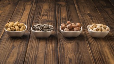 White ceramic bowls with nuts and seeds on a wooden table. A mixture of nuts and seeds.