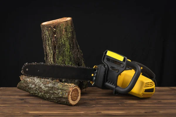 Two sawn logs and an electric chain saw on a wooden background. Electric tool for wood processing.