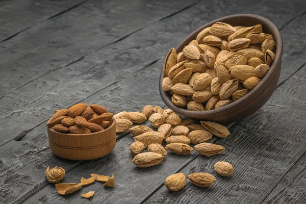 A small cup with peeled almonds and a large clay bowl with unpeeled almonds spilling out. Vegetarian food.