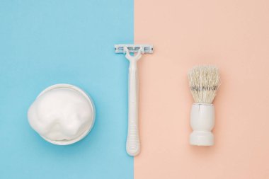 Tıraş köpüğü, beyaz jilet ve mavi ve bej arka planda beyaz fırça. Bir adamın yüzüne bakmaya hazır. Düz yatıyordu.