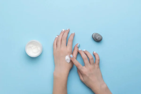 A beautiful stone, a jar of cream and a woman\'s hands on a blue background. Hand skin care. Flat lay.