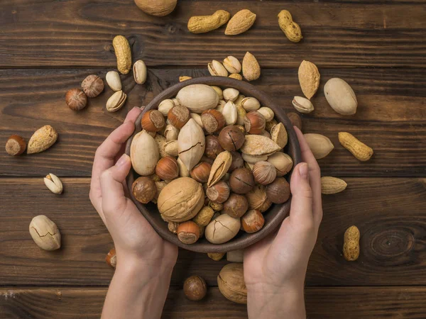 Nut mixture in a deep bowl in the hands of a woman over the table. Vegetarian food.