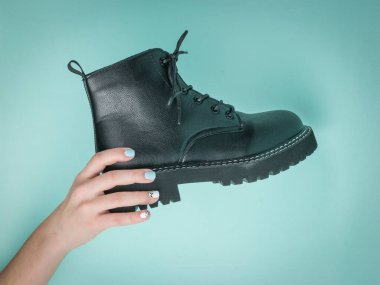 Bir kadının eli mavi arka planda siyah bir ayakkabı tutuyor. Sıradan ayakkabılar..