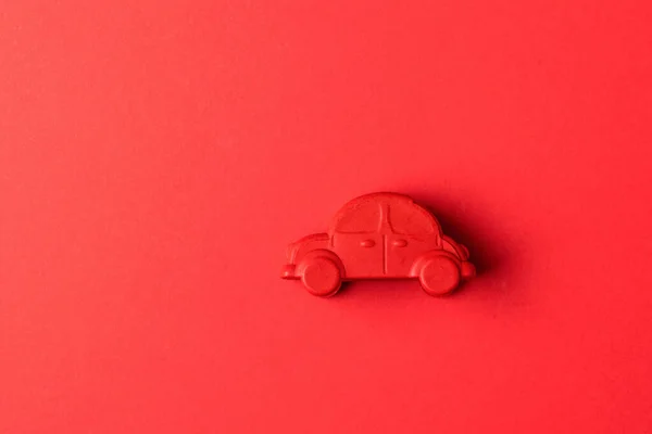 A small red toy car on a red background. The concept of selling and buying cars.