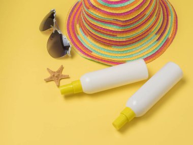 Two tubes of sunscreen, a hat and glasses on a yellow background. Taking a sun bath. Sun therapy.