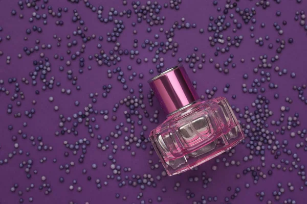 A bottle of perfume on a background of purple balloons on a purple background. Aromatic liquid.