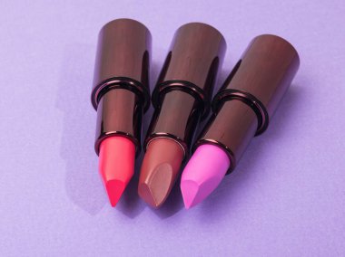 Mor arka planda farklı renklerde ruj tüpleri aç. Dudak dekorasyonu.