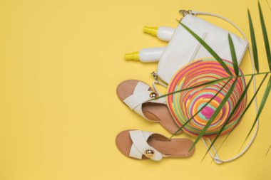 Sarı arka planda güneş kremi, şapka ve sandalet olan kadın çantası. Tatil konsepti. Düz yatıyordu.