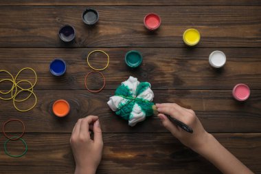 Bir kız kravat boyası tarzında beyaz bir tişört boyuyor. Renkli kumaş lekesi.