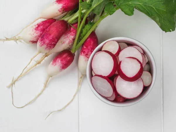 Whole and sliced radishes on a white wooden table. A fresh crop of radishes.