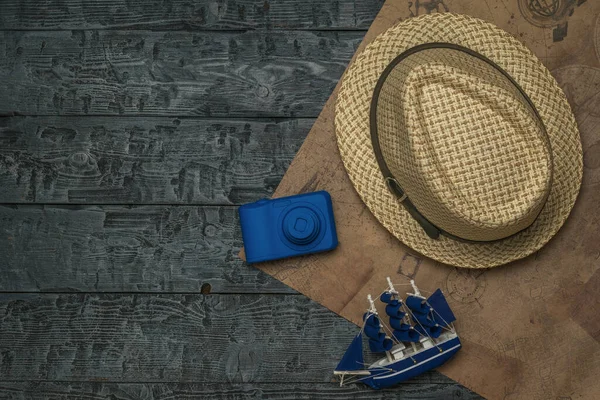 A hat, a model ship, and a camera on a piece of old paper on a wooden table. The concept of travel planning.