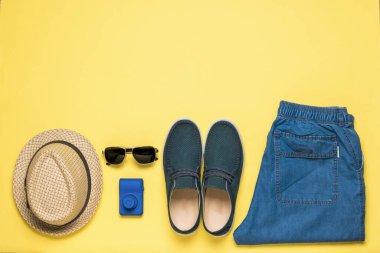 Sarı arka planda şapka, kot pantolon, ayakkabı, kamera ve gözlük. Metin için yer aç. Düz yatıyordu.