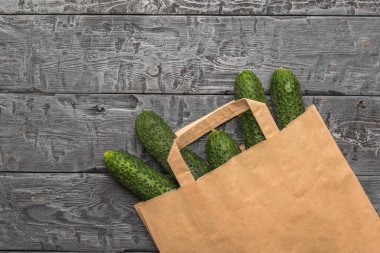 Tahta bir masada kağıt bir torbadan çıkan taze salatalıklar. Çevre dostu paketlerde taze sebzeler.