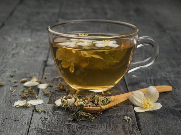 Herbal tea and flowers in a wooden spoon and a glass cup of tea. An invigorating drink that is good for your health.