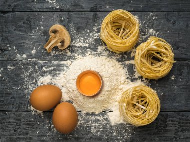 Tahta bir masada yumurta, un, mantar ve makarna. Makarna yapmak için gerekli malzemeler.