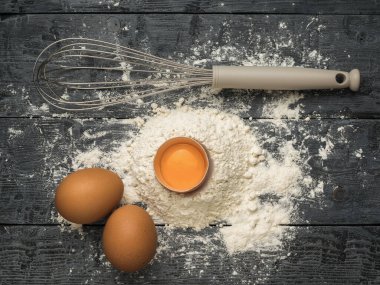 Tahta arka planda çırpmak için taze tavuk yumurtası, un ve çırpma çırpma. Doğal ürünler ve mutfak ekipmanları.
