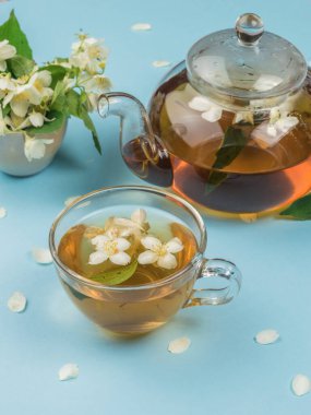 Mavi zemin üzerinde çiçek çayı olan bir bardak ve cam çaydanlık. Sağlığın için iyi olan canlandırıcı bir içecek..