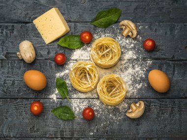 Siyah ahşap bir masada makarna, domates, mantar ve yumurta. Makarna yapmak için gerekli malzemeler.