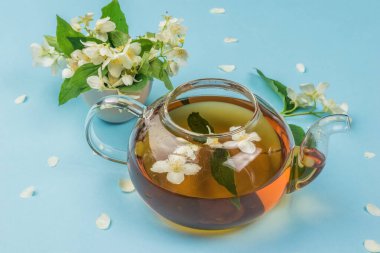Mavi arka planda çiçek çayı olan açık bir çaydanlık. Sağlığın için iyi olan canlandırıcı bir içecek..