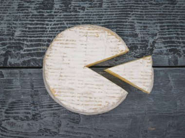 Camembert cheese with a cut piece on a wooden table. A product made from natural milk.