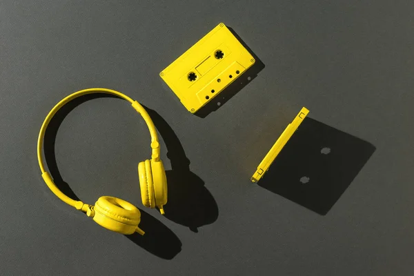 两个带磁带和黄色耳机的盒式磁带 明亮的灯光照射在灰色背景上 颜色趋势 听音乐的老式设备 平躺在床上 — 图库照片