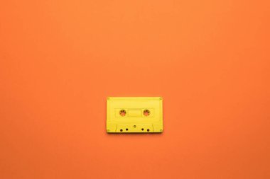 Turuncu arka planda manyetik bandı olan parlak sarı bir kaset. Müzik dinlemek için modaya uygun retro ekipmanlar. Düz yatıyordu.
