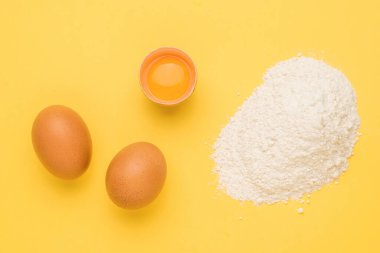 Parlak sarı arka planda buğday unu ve tavuk yumurtası. Doğal ürünler ve mutfak ekipmanları.