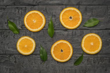 Pieces of fresh orange and leaves on a black wooden table. A popular tropical fruit. Flat lay.