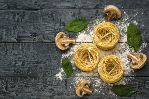 三根意大利面 三半蘑菇和菠菜叶子在一张木制桌子上 做意大利面的配料 案文的位置 — 图库照片