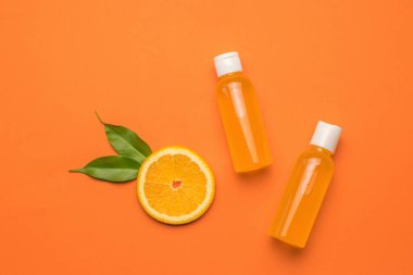 A piece of orange with leaves and two bottles of juice on an orange background. The concept of therapy with natural remedies. Flat lay.