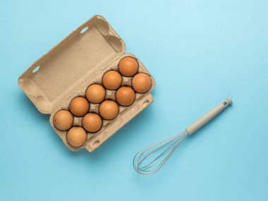 An open box with eggs and a whisk for whipping on a blue background. Natural products and kitchen equipment.