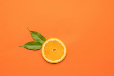 Turuncu arka planda iki yaprak ve bir parça portakal. Popüler bir tropikal meyve. Düz yatıyordu.