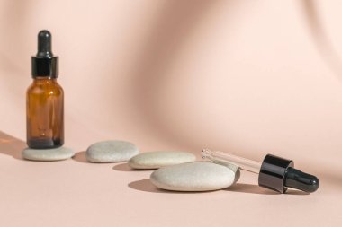 Bitkilerin gölgesinde bej bir arka planda pipetli ve taşlı şişeler. Doğal tedavi ve vücut bakımı kavramı.