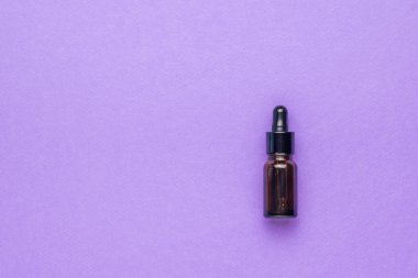 Mor arka planda pipeti olan küçük bir tıbbi şişe. Doğal tedavi ve vücut bakımı kavramı. Düz yatıyordu.