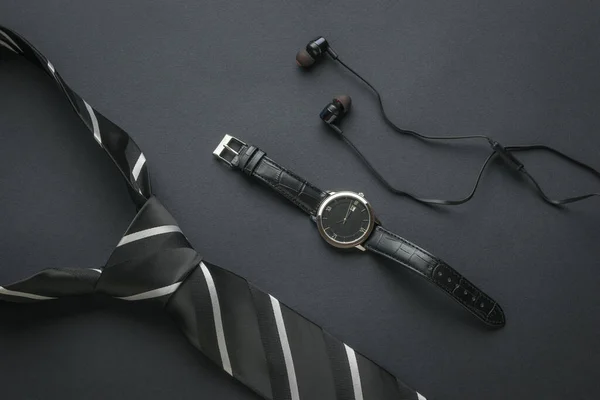Men\'s watch with hands, headphones and a tied tie on a black background. Subjects for men.