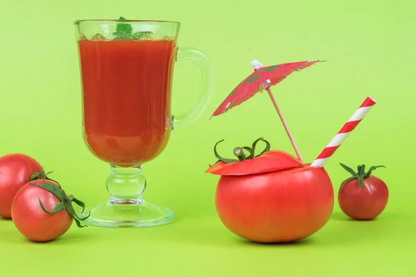Sliced tomato with a cocktail tube, a glass of tomato juice and scattered tomatoes on a green background. The concept of consumption of fresh vegetable juice.