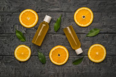 Siyah ahşap bir masada iki şişe portakal suyu, yapraklar ve portakal dilimleri. Doğal ilaçlarla terapi kavramı..