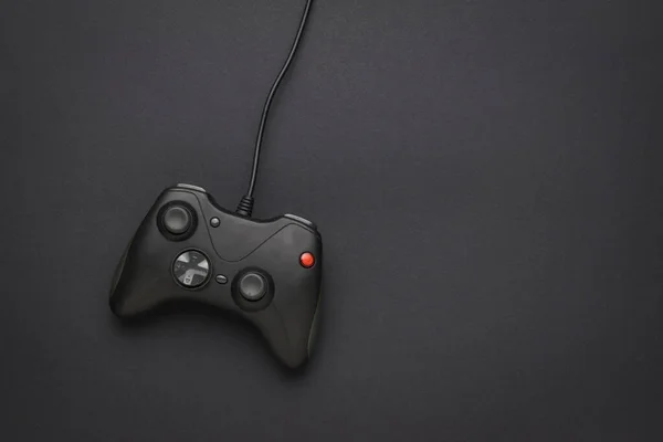 A black game console with a wire on a black background. A device for playing computer games. Flat lay.