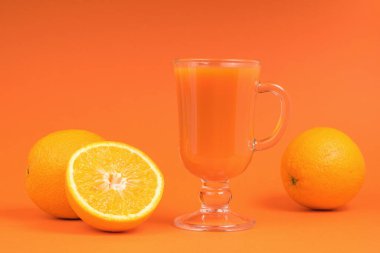 Turuncu arka planda taze sıkılmış meyve suyu ve portakallar. Besleyici bir vejetaryen içeceği..