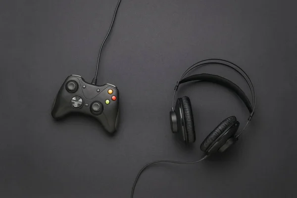 Wired headphones and a wired game console on a black background. A device for playing computer games. Flat lay. Place for text.