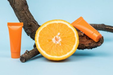 Bir parça portakal, eski bir ağaç ve mavi arka planda iki turuncu krema. Doğal minerallere dayanan kozmetik ve tedavi amaçlı merhem.