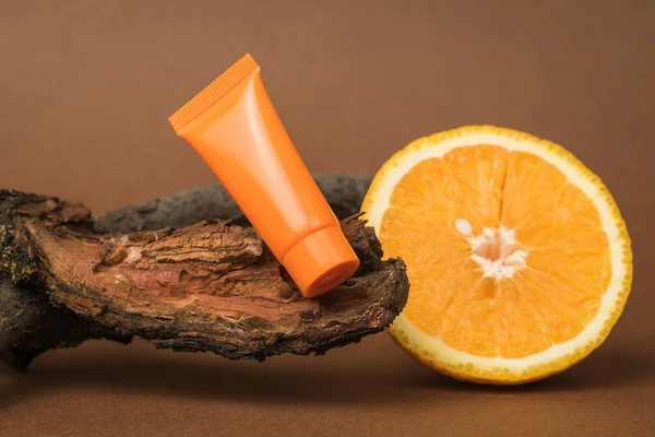 A sliced orange, an orange tube of cream and a branch of an old tree. Cosmetics and therapeutic ointments based on natural minerals.