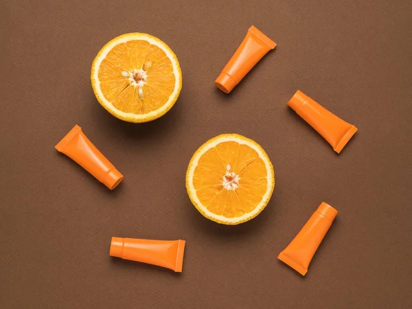 Two halves of an orange and five tubes of cream on a brown background. Cosmetics and therapeutic ointments based on natural minerals. Flat lay.